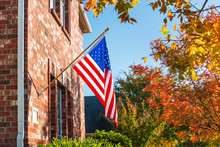 Patriotic American Flag Waving In Front Of A Brick Home On A Sunny Autumn Day.