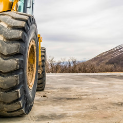 Wall Mural - Square Close up of the tires of a bulldozer against snow peaked mountain and cloudy sky