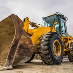 Wall Mural - Square Side view of a yellow bulldozer with dirty metal bucket and black rubber wheels