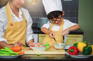 Wall Mural - Asian woman young mother with son boy cooking salad mom sliced vegetables food son tasting salad dressing vegetable carrots and tomatoes bell peppers happy family cook food enjoyment lifestyle kitchen