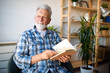 © NDABCREATIVITY - Happy senior man reading book at home