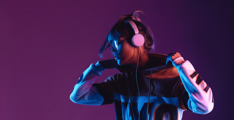 Wall Mural - Hipster igen teen pretty fashion girl model wear stylish glasses headphones enjoy listen new cool music mix stand at purple studio background in trendy 80s 90s club blue party light, profile view