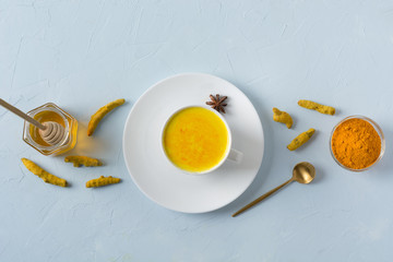 Wall Mural - Cup of ayurvedic golden turmeric latte milk with curcuma powder on blue. View from above.