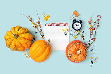 autumn composition with empty notepad, orange pumpkins, alarm clock, paper clips and buttons on blue