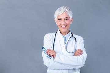 Portrait of senior female doctor with stethoscope & arm cross isolated on background. The physician standing with cheerful gesturing. She wearing doctor uniform in hospital. Health insurance concept.