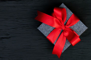 Wall Mural - gift box Dark gray new year  Packed present container with red ribbon on Vintage Matte black wooden board background for holiday concept with copy space, top view.