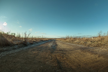 Country road through a autumn field among dried grass background.