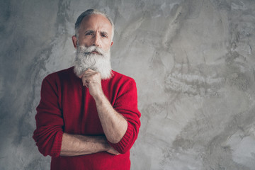 Photo of attractive white haired aged guy holding hand chin look clever eyes minded wear red knitted pullover hipster santa clothes isolated grey color concrete wall background