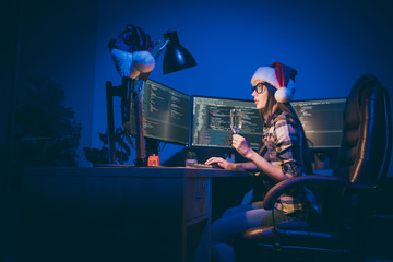 Profile photo of programmer lady with sparkling wine glass watching screen working late night meet newyear alone at dark office workaholic wear santa cap indoors
