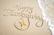 © PeskyMonkey - Happy Thanksgiving message handwritten on smooth sand beach with decorative starfish and oncoming wave