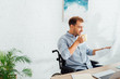 © LIGHTFIELD STUDIOS - Smiling man in wheelchair drinking tea and reading newspaper at desk