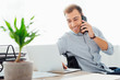 © LIGHTFIELD STUDIOS - Smiling freelancer talking on smartphone and using laptop at desk