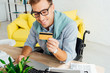 © LIGHTFIELD STUDIOS - Smiling man in wheelchair looking at credit card and using laptop at table