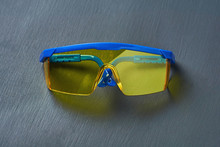 Ski Goggles Or Modern Protective Glasses For Worker On Building, Welder, Dentist, Turner And Other With Yellow Glass And Blue Frame Lies On Dark Concrete Desk. Close-up