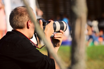 Photographer with a camera while working. A man photographs a competition. Free space, close-up, horizontal, side view. A concept of a hobby and profession.