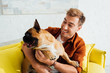© LIGHTFIELD STUDIOS - Smiling man hugging french bulldog on sofa