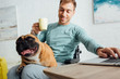 © LIGHTFIELD STUDIOS - Disabled man holding french bulldog on knees while drinking tea and working on laptop