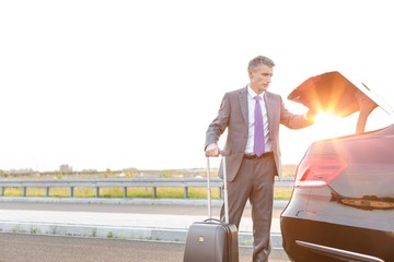 Wall Mural - Businessman standing at car trunk and getting his suitcase