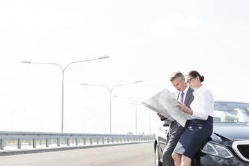 Wall Mural - Business professionals analyzing map outside car on road against sky