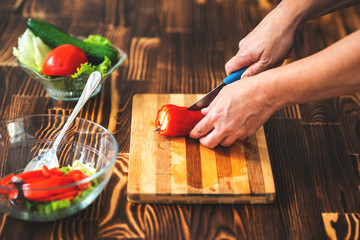 Young woman is cutting paprika on cutting board for salad