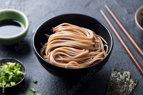 Cuadros en Lienzo Soba noodles on a black bowl. Slate background. Close up.