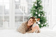© VK Studio - Festive mood, friendship, love between people and animals. Pleased smiling brunette woman in warm sweater hugs pet with love, enjoys spending time at home, prepares for Christmas celebration