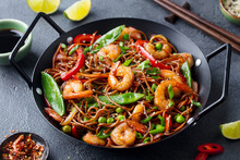 Stir Fry Noodles With Vegetables And Shrimps In Black Iron Pan. Dark Background. Close Up.