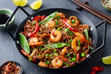 Stir fry noodles with vegetables and shrimps in black iron pan. Dark background. Close up.