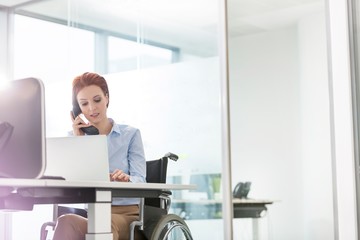 Wall Mural - Businesswoman sitting on wheel chair while working in office