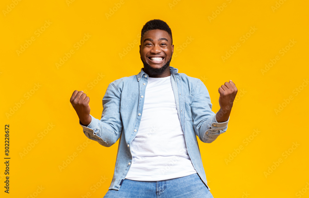 Portrait of overjoyed black man celebrating success with clenched fists - obrazy, fototapety, plakaty 