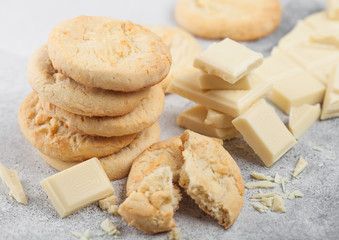 White chocolate biscuit cookies with chocolate blocks and curls on light kitchen table background.