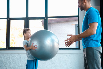 Poster - cute kid holding fitness ball and looking at father in gym