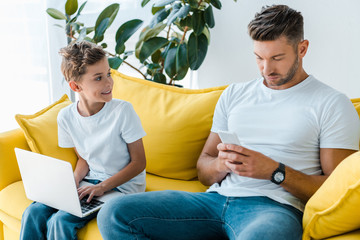 Poster - cute son with laptop looking at father using smartphone at home