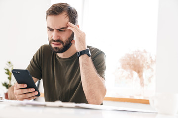 Canvas Print - Image of caucasian tired man typing on cellphone while sitting