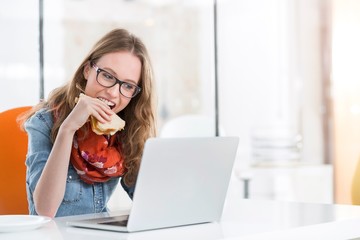 Young entrepreneur eating sandwich while working in office