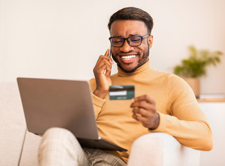 Wall Mural - Man talking on cellphone using credit card and laptop indoor