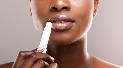 Wall Mural - Black woman applying lip balm over grey background, closeup