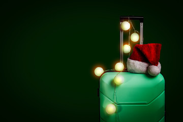 Plastic suitcase, Santa Claus cap and garland on a dark green background. Concept of travel, business trips, trips to visit friends and relatives on Christmas holidays. New Years journey