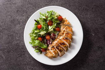 Poster - Grilled chicken breast with vegetables on a plate on black background. Top view