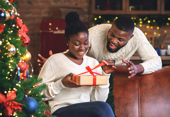 Wall Mural - Excited afro girl opening Christmas gift from her boyfriend