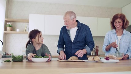 Sticker - A small girl with senior grandparents indoors in kitchen preparing food.