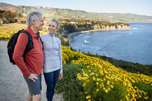 Smiling Senior Woman Looking At Man While Standing By Flowering Plants On Cliff At Beach
