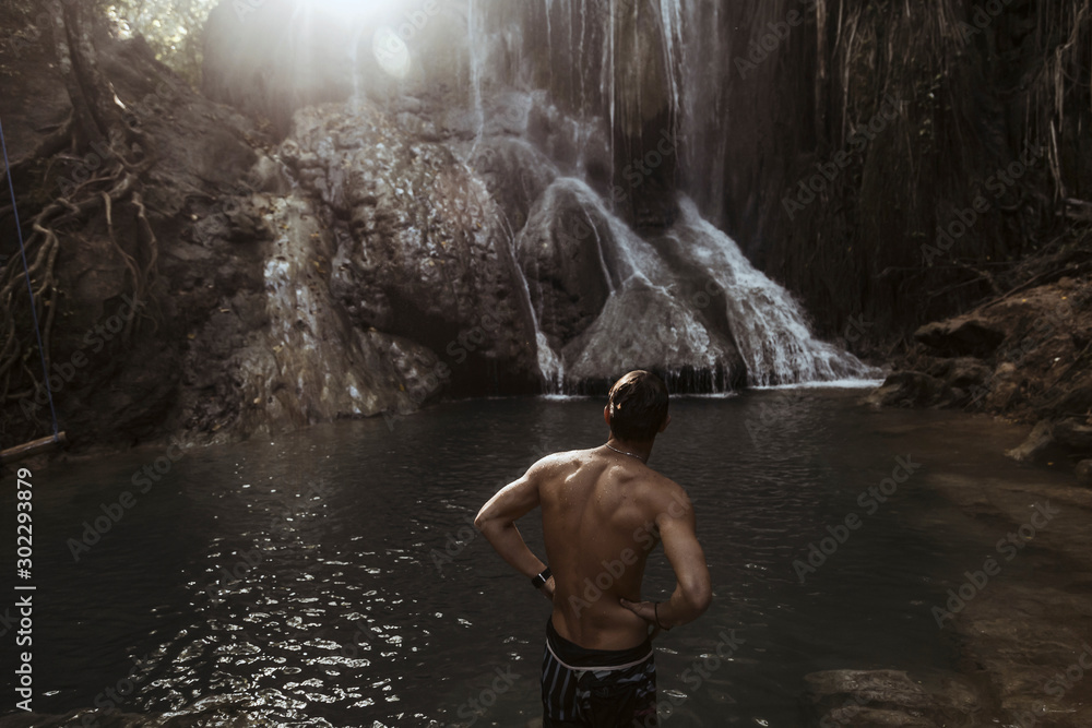 Rear view of shirtless man standing at waterfall Stock Photo | Adobe Stock