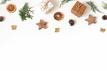 Christmas Floral Frame, Web Banner. Garland Of Juniperus, Cypress Branches, Pine Cones, Gift Boxes, Wooden Stars And Dry Orange Fruit On White Background. Winter Design And Decoration. Flat Lay, Top.