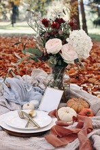 Autumn Wedding Table Setting. Garden Party Celebration, Picnic With Golden Cutlery, Porcelain Plate,wine Glass And White Pumkins. Rose Flowers Bouquet With Olive Branches. Red Beech Leaves Ground.
