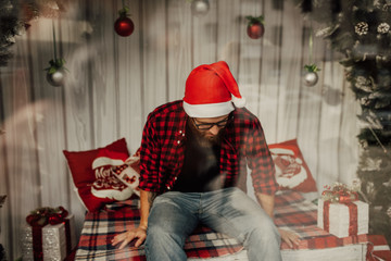 Unhappy and sad young man in a Santa Claus hat sits alone on a decorated Christmas location