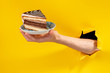 © yuriygolub - Hand offering a piece of cake through a torn hole in yellow paper background.