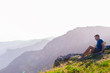 © qunica.com - Adventurous man sitting on top of a mountain and enjoying the beautiful view, while looking downhill at the blue river and amazing mountain line..