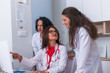© qunica.com - ( Medical Team ) Female doctor ( medic ) in her 30's working on her computer while two female nurses stand next to her and discuss a patients illness...