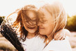 © Strelciuc - Close up portrait of a lovely little girl embracing her mother smiling outdoor against sunset while wind blowing their hair.